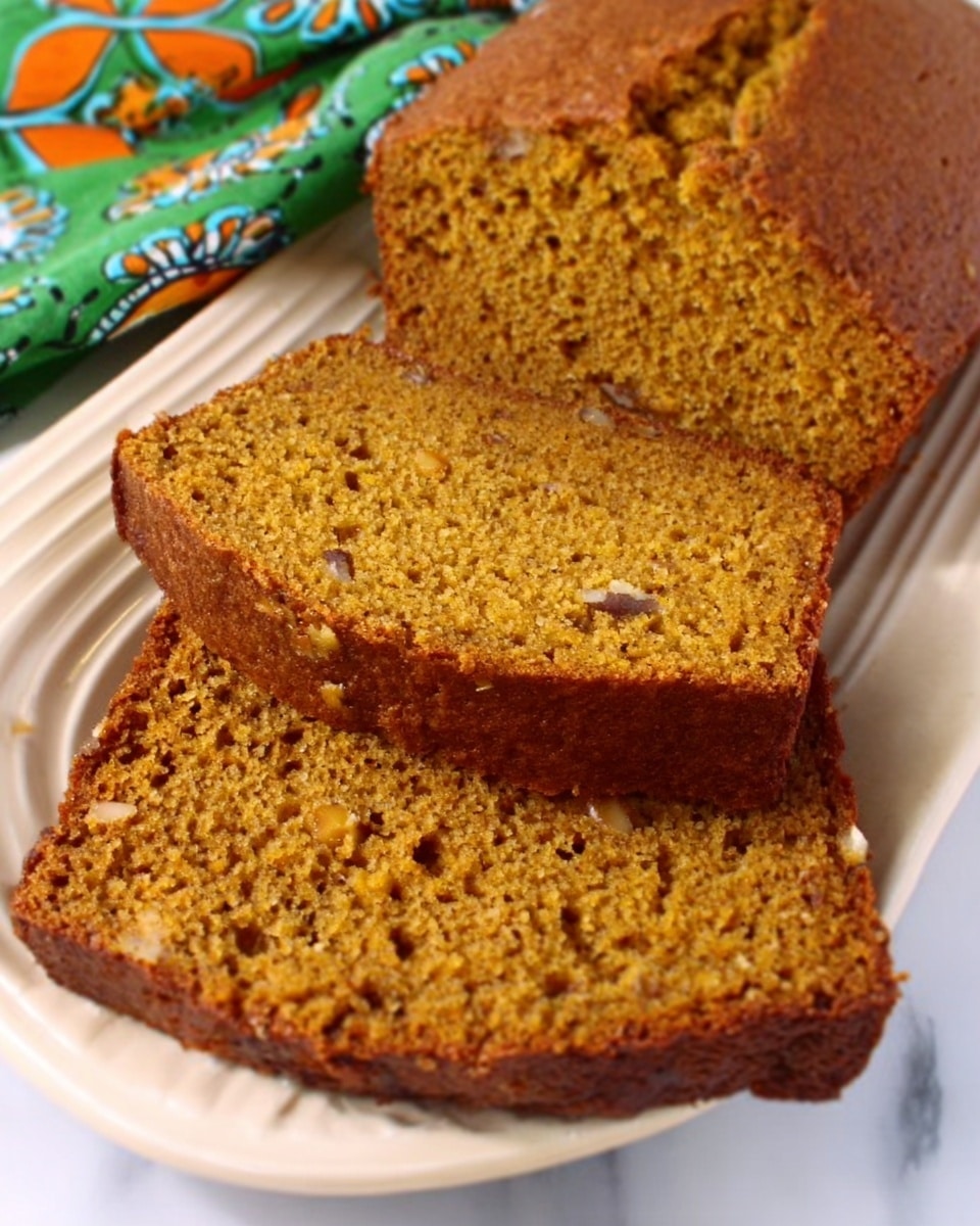 A loaf of pumpkin bread is shown sliced, with three pieces neatly placed in front of the remaining loaf. The bread has a moist, dense texture with visible small bits of nuts or spices inside, with a golden-brown color on the outside and a slightly darker inside. The slices rest on a white plate that has a subtle curved edge design. Underneath the plate, there is a white marbled surface. The background includes a colorful cloth with green, orange, and blue patterns. photo taken with an iphone --ar 4:5 --v 7