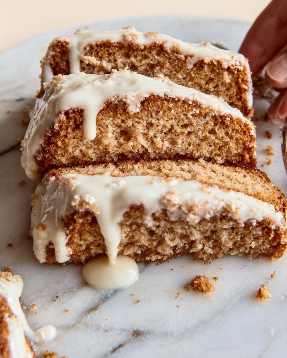The image shows a close-up of three layered slices of light brown cake with a crumbly texture, each topped with a smooth, creamy white icing that softly drips down the sides. The slices are placed closely together on a white marbled surface, with small crumbs scattered around them. A woman's hand is partially visible on the right, gently touching one of the slices. Photo taken with an iphone --ar 4:5 --v 7